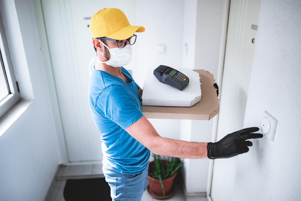 a food deliveryman holds pizza boxes and rings a doorbell at a person's residence