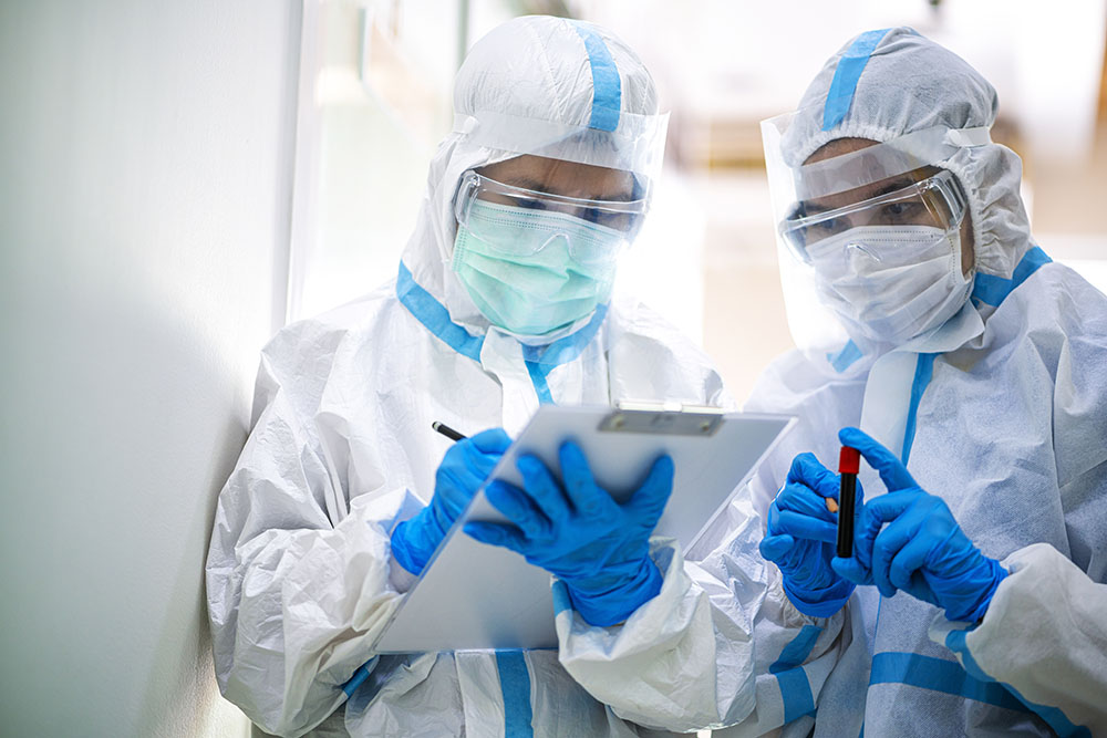 two people dressed in PPE hold  tubes full of blood and take notes
