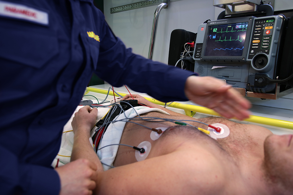 an EMT in an ambulance places nodes on a patient's chest to check their heart rate