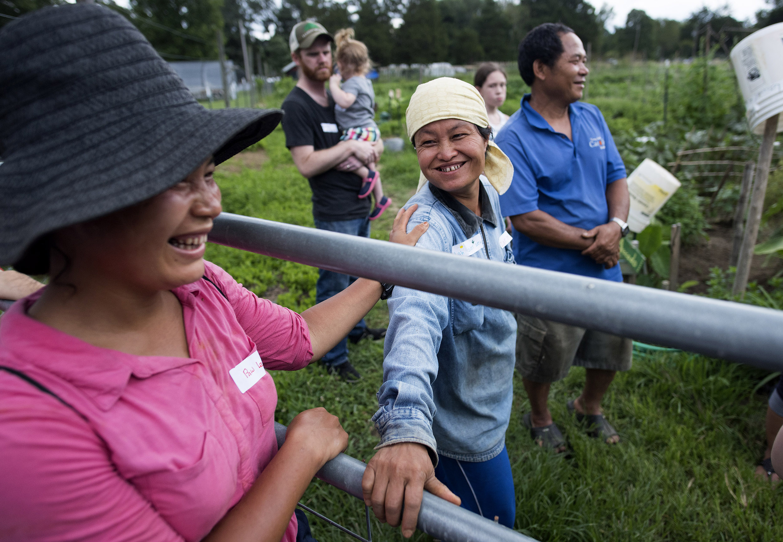 two Karen women stand on each side of a fence; both laugh and one puts her hand on the other's shoulder