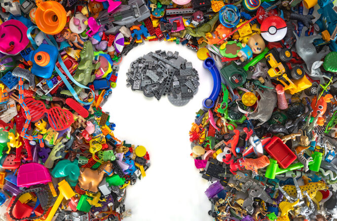 Plastic toys in various colors are arranged to form the shape of a child's head and shoulders, while gray toy building bricks are used to depict the child's brain.