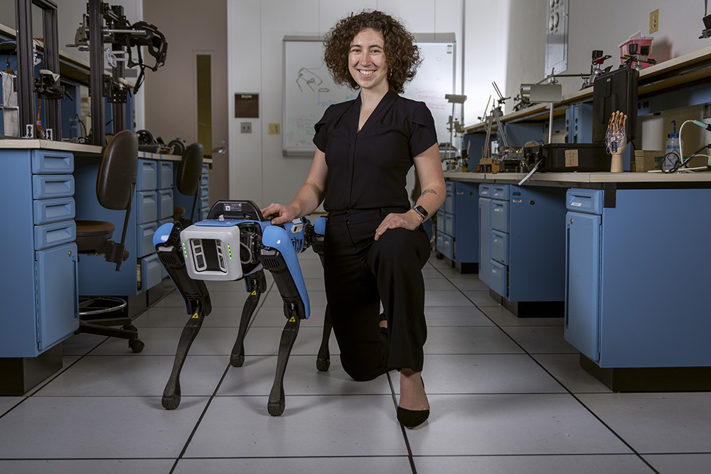 Lilly Nekervis, a senior undergraduate students, majoring in Information and Library Science at UNC-Chapel Hill, poses with a robotic dog in a robotics lab.