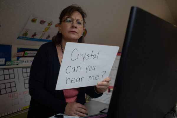 Suzanne Zaccardo holds up a sign in front of her computer that says "Crystal can you hear me?"