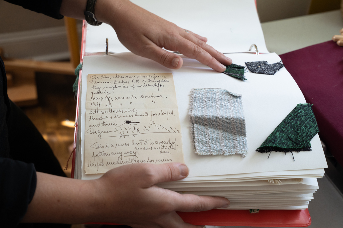 Photo: A pair of hands holding a large scrapbook. The book is open to a page containing several woven fabric samples and a handwritten note.