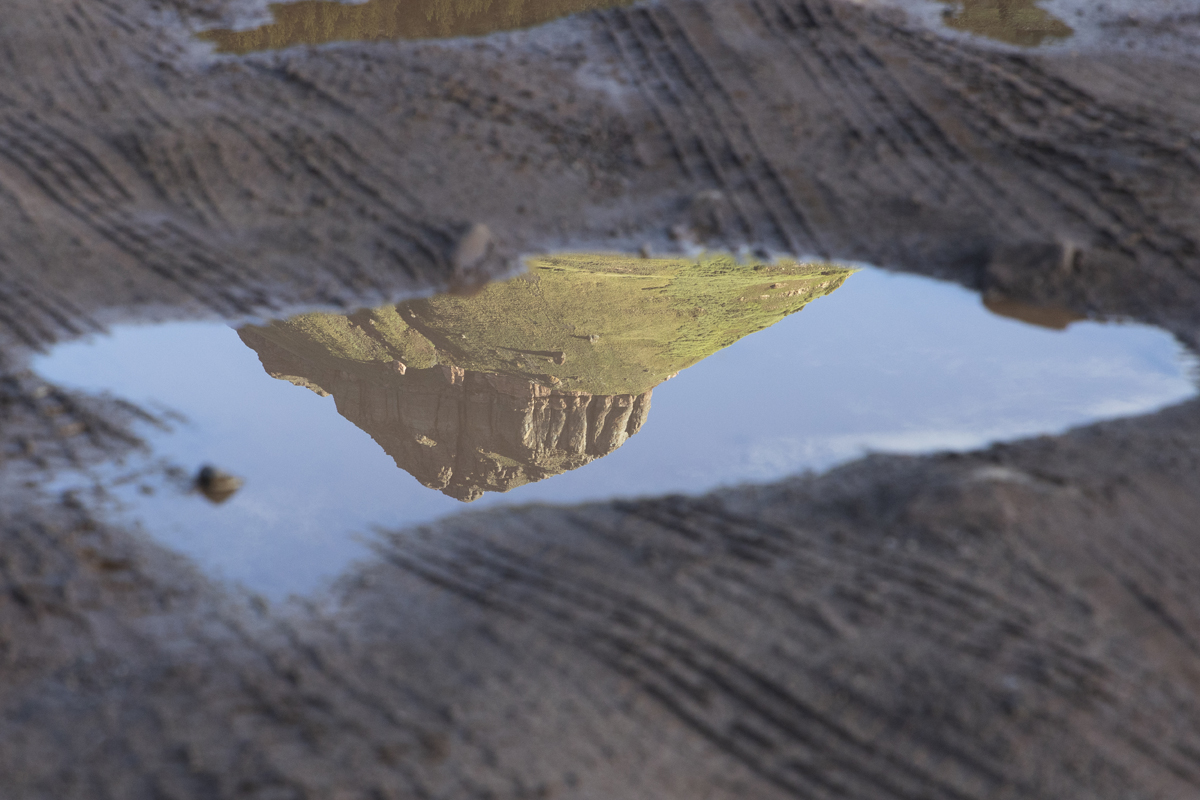 A view of a mountain top near Spencer Peak reflects in a parking lot puddle