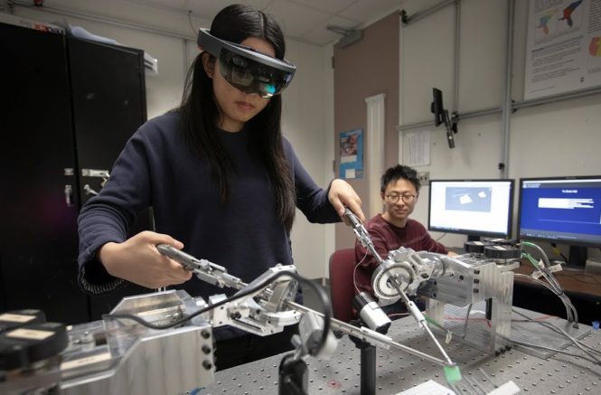 a girl wears an augmented reality headset while controlling long rods on a simulator that mimics laparoscopic surgery