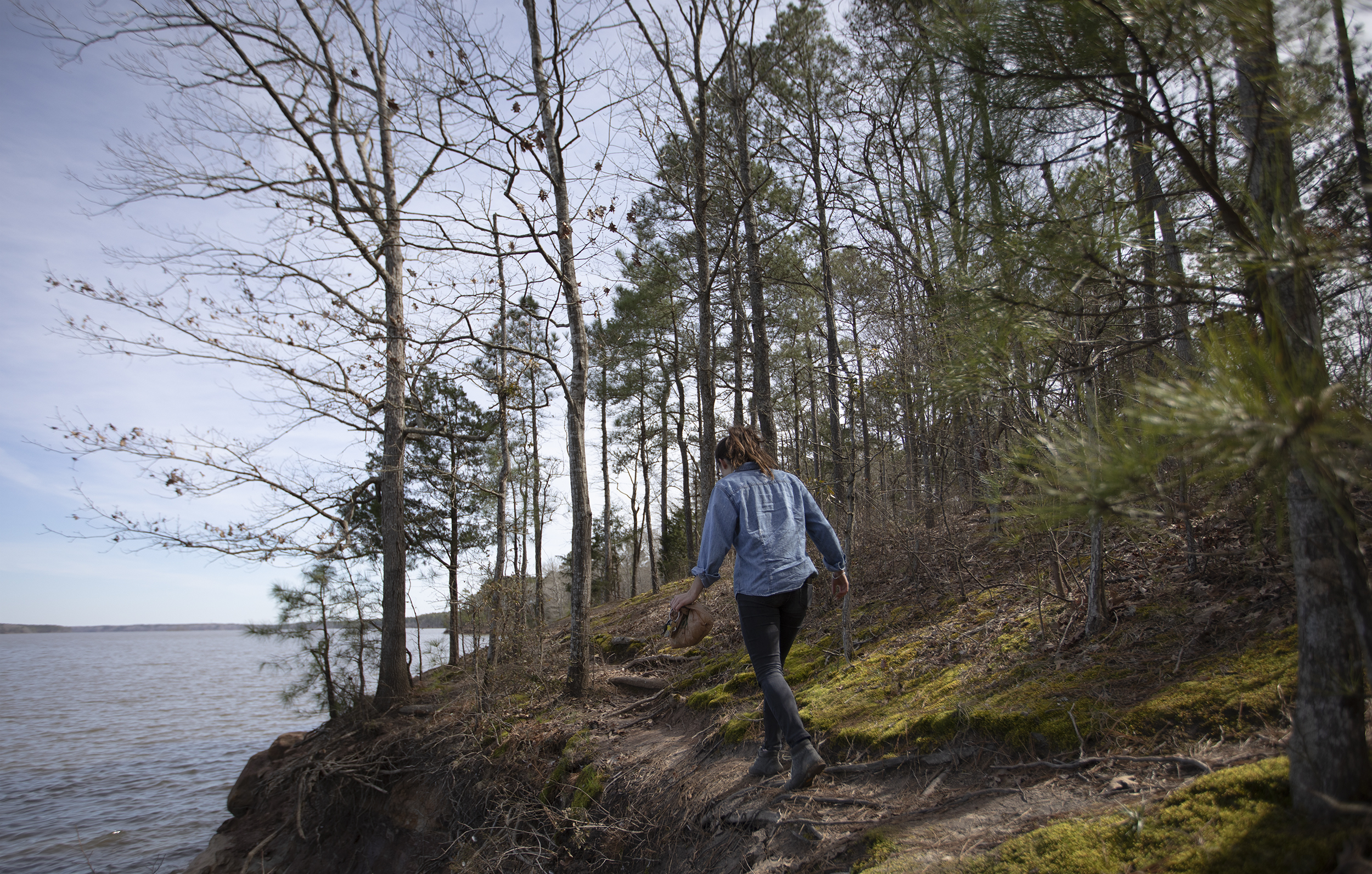 Ayla Gizlice walks along an elevated shoreline among trees at Jordan Lake.