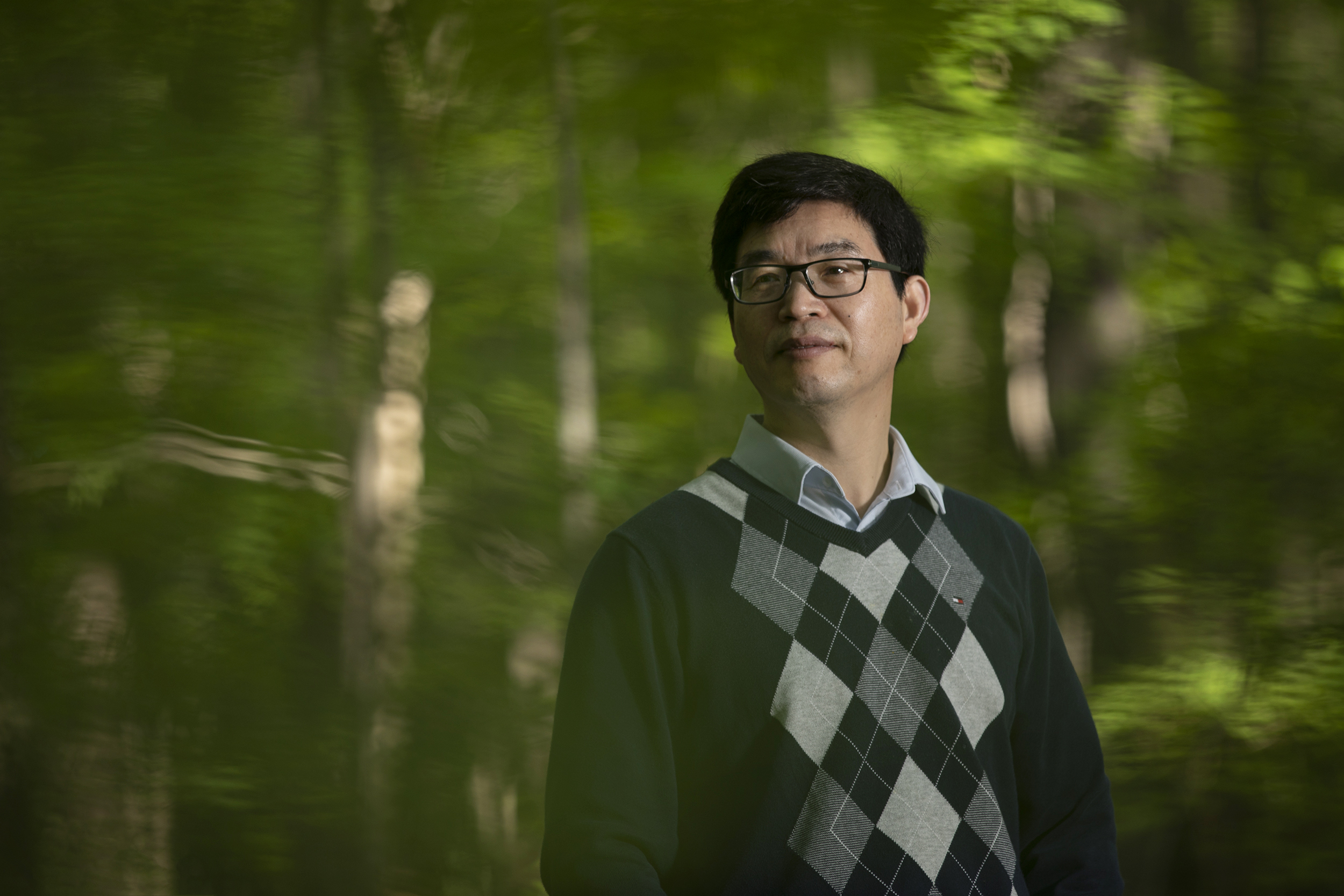 Conghe Song stands for a portrait in a forest.