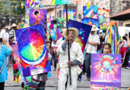 an elderly man and two young girls hold colorful signs while walking down a street in Mexico