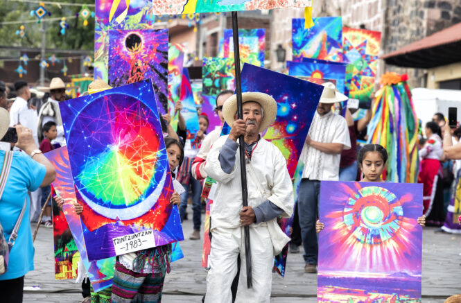 an elderly man and two young girls hold colorful signs while walking down a street in Mexico