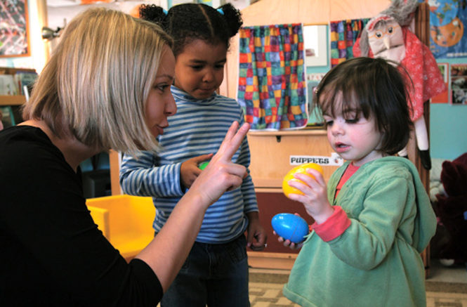 a blond woman holds two fingers up to a toddler, trying to teach her how to count