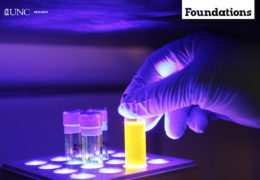 a blacklight makes everything purple while a gloved hand places a test tube full of yellow fluid into a a test tube tray