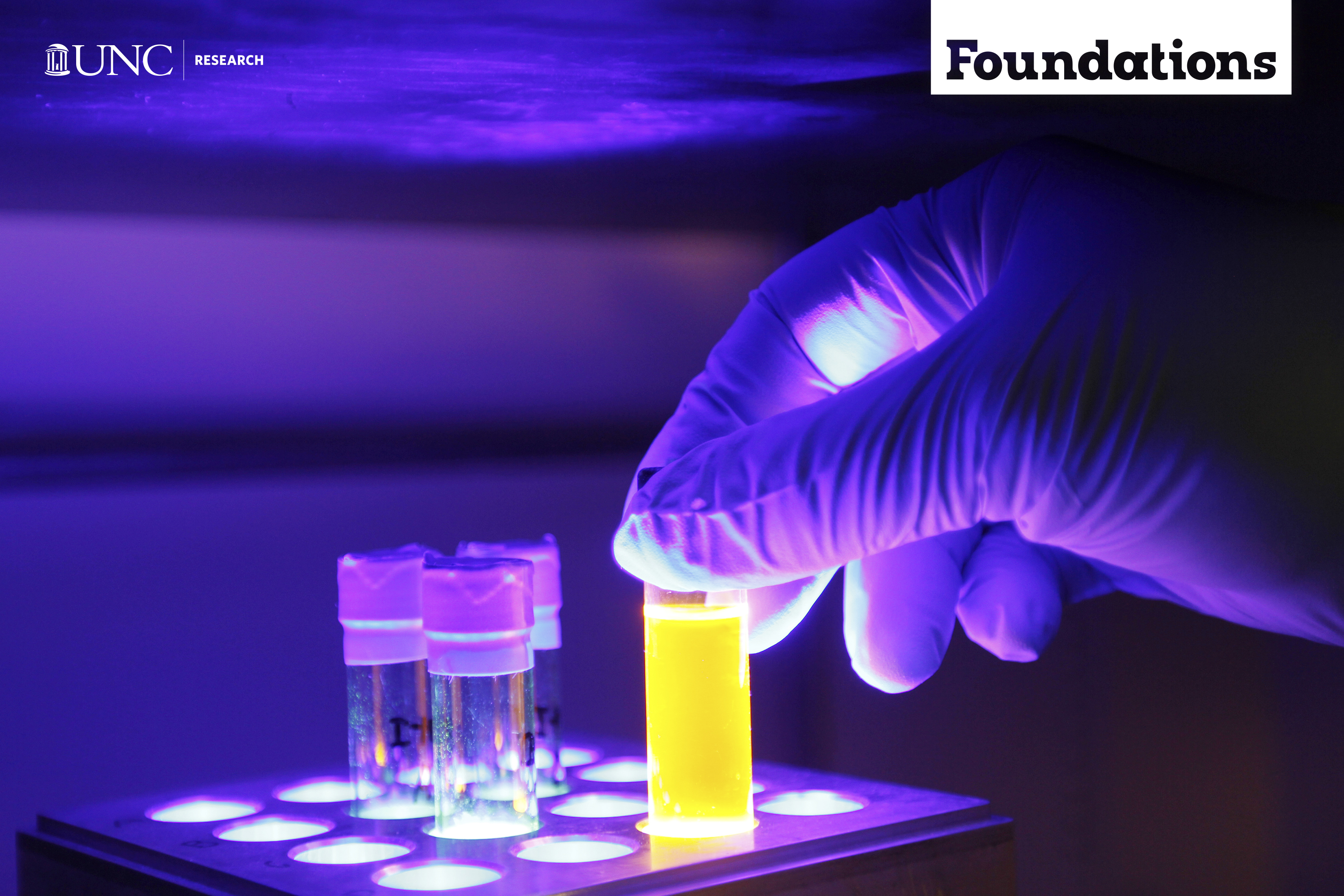 a blacklight makes everything purple while a gloved hand places a test tube full of yellow fluid into a a test tube tray