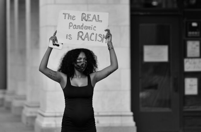 a woman holds a sign that reads "the real pandemic is racism"