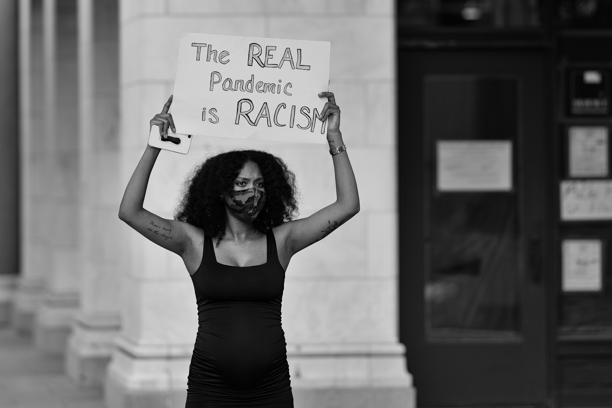 a woman holds a sign that reads "the real pandemic is racism"