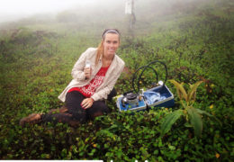 Sarah Schmitt sits in a field with her research equipment, smiling at the camera.
