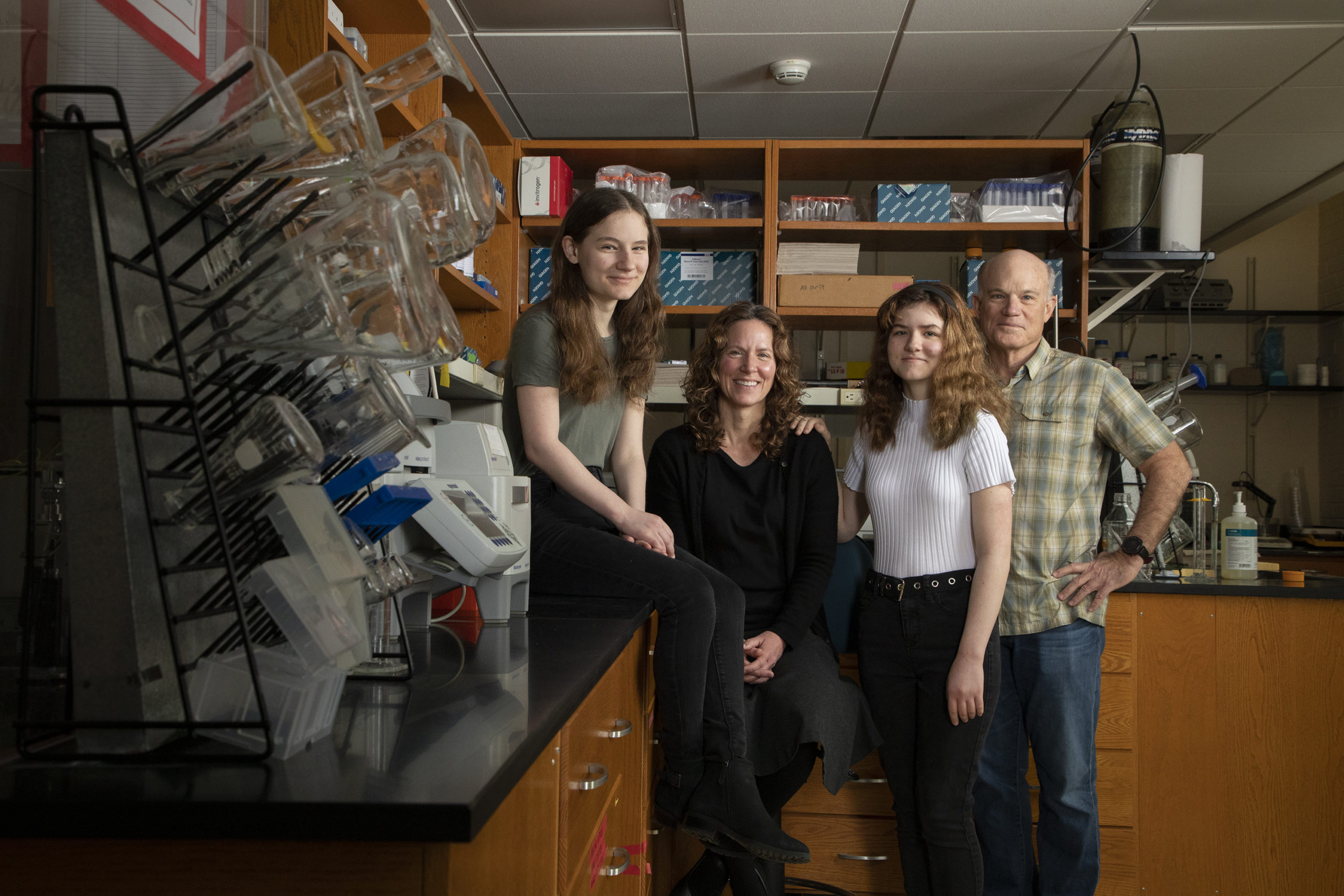 A mother, father, and two daughters pose for a portrait inside a university laboratory space.