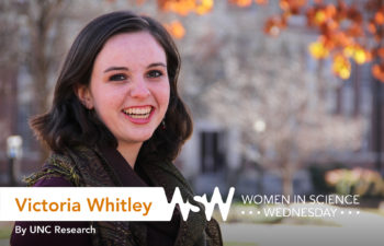 a 20-something female stands in front of a autumn-orange tree and smiles at the camera