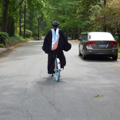 Alice Ammerman in cap and gown riding a Carolina blue bike down the street