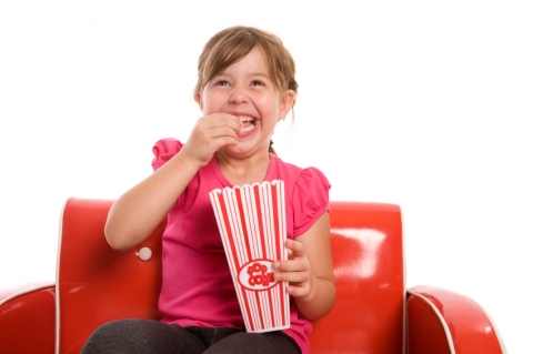 Little girl sits in chair with a box of popcorn, smiling