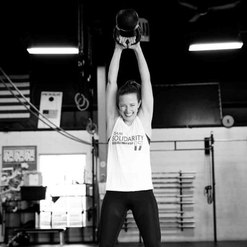 a girl in spandex and a tank top lifts a weighted exercise ball over her head