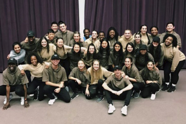 a group of 20-plus students on the hip hop dance team pose for a photo in front of a curtain