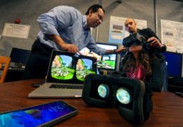 Photo of Dinesh Manocha and Carl Schissler help someone testing out their VR-headphones display.
