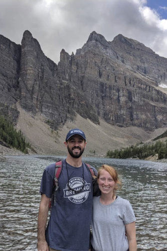 Emma Marzolf and her husband Nick pose in front of a glacial lake and mountains