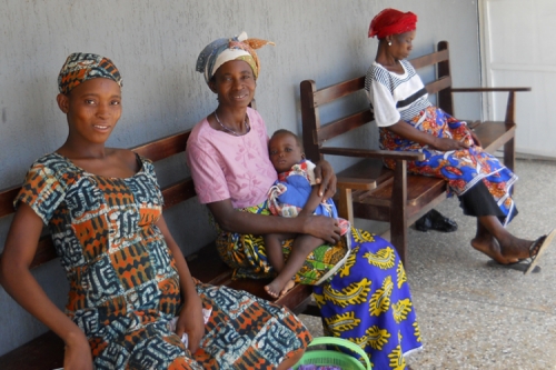 Woman in daily Ghana clothing, sit on a bench outside.