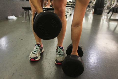 Showing one someones legs and feet, they stoop down to pick up two 40 pound hand weights