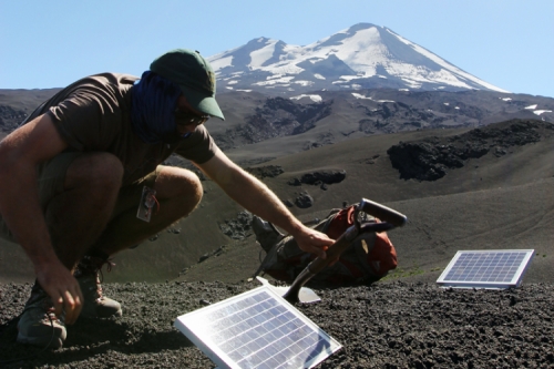 Photo of Tim Ronan burying a cable to a solar panel into the dirt, overlooking the Llaima volcano.