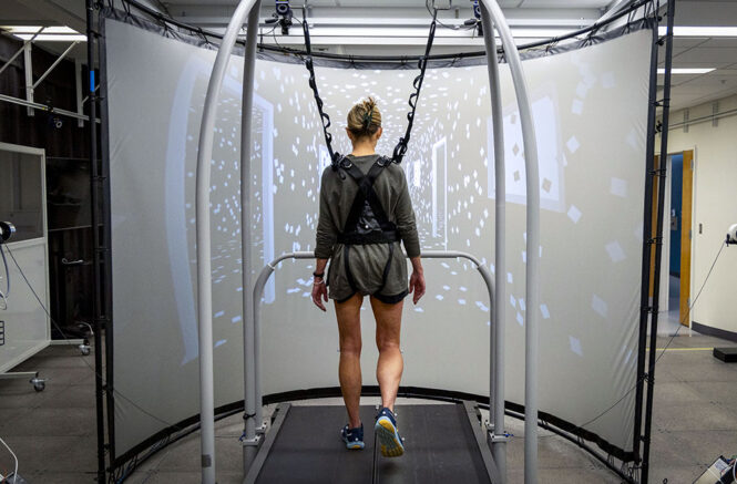 A woman wears a harness while walking on a treadmill in a lab