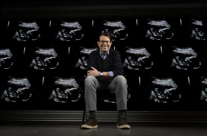 Jeff Stringer in front of a screen covered in pregnancy ultrasounds