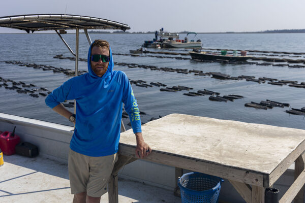 a man stands on a boat floating near an oyster farm