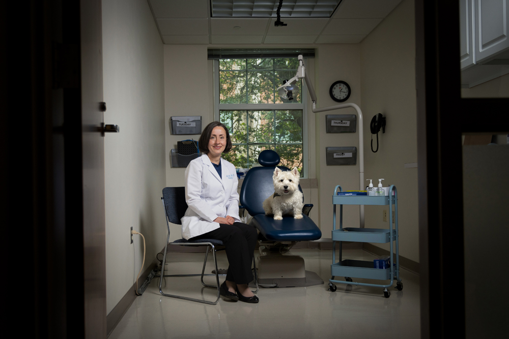 Laura Jacox sits next to Sugar, the therapy dog, in a dentist-like room