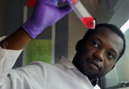 Photo of Moses Bility in the lab looking at a test tube.