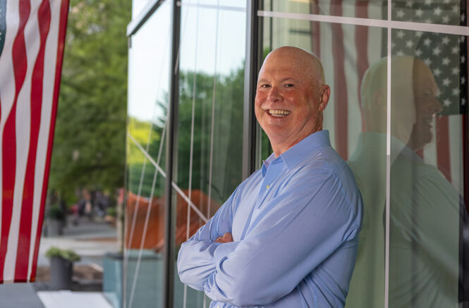 a man leans against a window with a reflection of an American flag in it