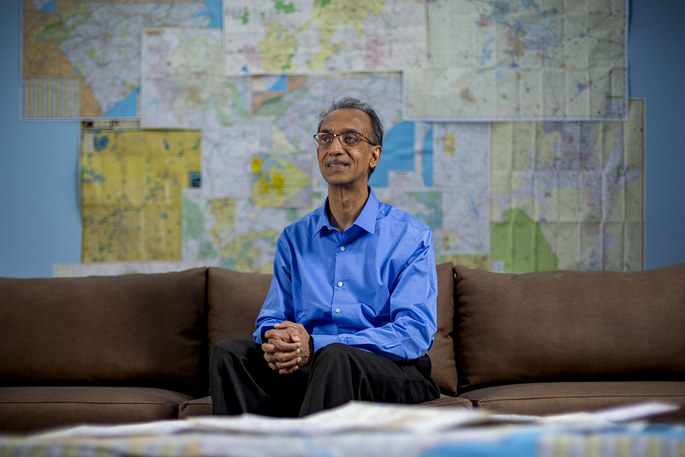 A man sits on a couch in front of a wall filled with maps.