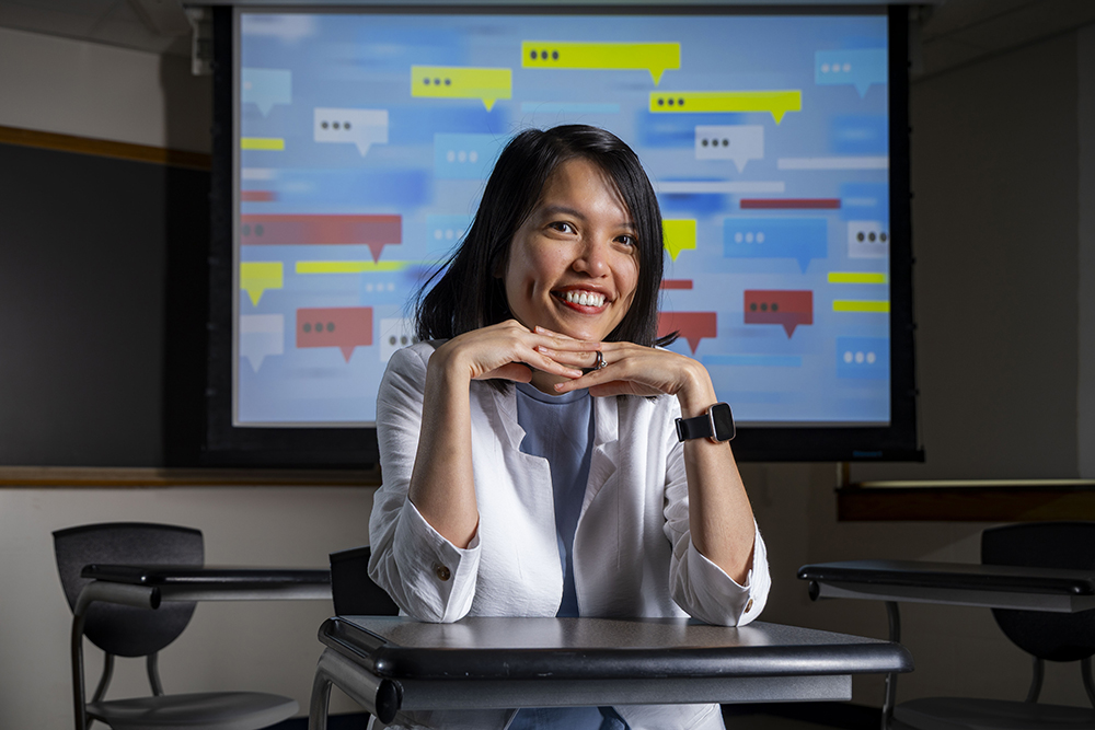 A women sits at a desk infront of a projected image of a text conversation.