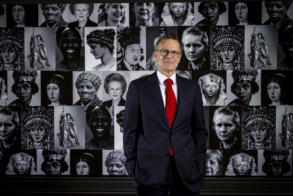 A male professor stands in front of a screen displaying photos of famous female leaders.