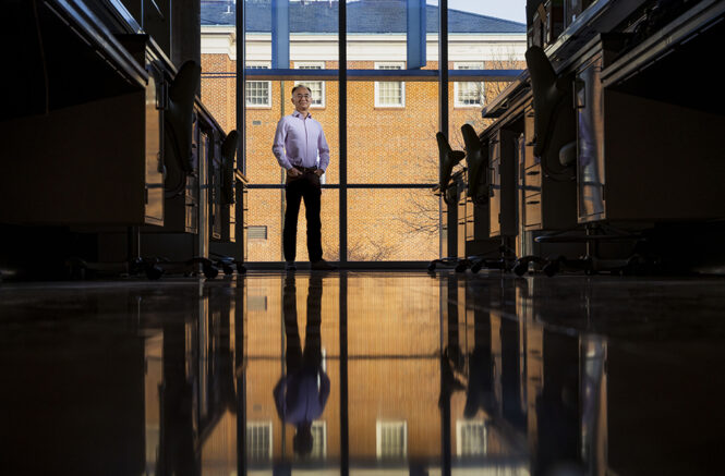 Wei You stands in a chemistry lab, and his reflection is mirrored on the shiny concrete floor.