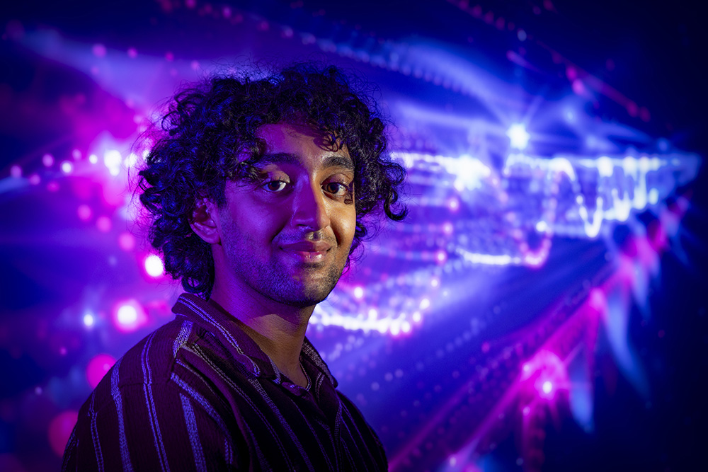 A male student poses in front of a projection of a wave form.