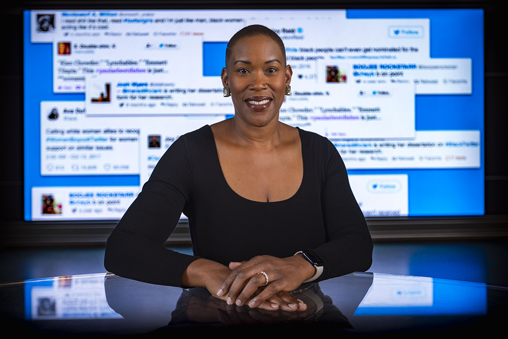 A female professor stands in front of a screen displaying tweets from black twitter.